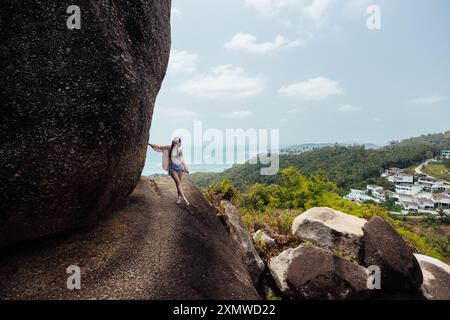 Une femme se tient près d'un grand rocher sur une colline surplombant la côte de Koh Samui. L'île est visible en arrière-plan, avec l'eau turquoise Banque D'Images