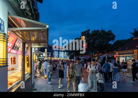 suzhou, Chine - 10 juin 2024 : scène de rue en soirée à Suzhou, Chine, avec des gens marchant devant des magasins et des stands de nourriture. Banque D'Images