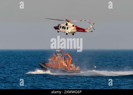 Weymouth, Dorset, Royaume-Uni. 29 juillet 2024. Le Severn Class RNLI Lifeboat RNLB Ernest and Mabel fait une exposition en soirée pour le public au large de la côte à Nothe Gardens pendant la journée de plaisir des organismes de bienfaisance pendant la semaine du bateau de sauvetage à Weymouth dans le Dorset. Un avantage supplémentaire pour les spectateurs a été l'apparition imprévue de l'hélicoptère des garde-côtes de Lee on Solent qui a treuillé un membre de l'équipage de l'hélicoptère du pont du bateau de sauvetage après qu'il a été appelé dans la région pour effectuer une fouille de la côte de Portland. Crédit photo : Graham Hunt/Alamy Live News Banque D'Images