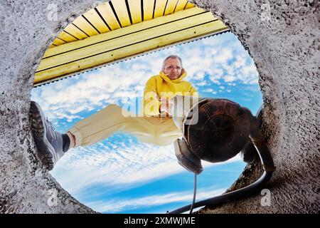 Pompage de fosse septique en utilisant la pompe submersible d'eaux usées, le propriétaire de la maison immerge l'équipement dans les eaux usées à travers le trou dans l'anneau de béton du puits. Banque D'Images