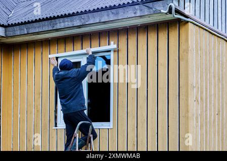 Travaux de finition extérieure sur le cadre et la maison de panneaux côté façade, couvreur installe des montants d'ouverture de fenêtre. Banque D'Images