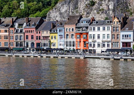 Paysage urbain de Dinant station balnéaire, bâtiments colorés contre mur de montagne rocheux, terrasses touristiques de restaurants sur la promenade le long de la rivière Meuse, soleil Banque D'Images