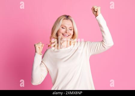 Photo de joyeuse heureuse belle femme senior habillée des vêtements élégants isolés sur fond de couleur rose Banque D'Images