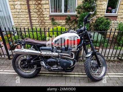 Une moto Triumph Bonneville est garée devant un immeuble résidentiel avec des murs en pierre et une clôture en fer forgé noir. Calne Bike Meet 2024 Banque D'Images