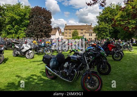 Un rassemblement de motos en plein air pittoresque, avec de nombreuses motos garées sur l'herbe et un bâtiment historique en arrière-plan. Calne Bike Meet 2024 Banque D'Images