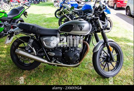 Une élégante moto Triumph Street Twin noire et argentée garée sur une zone herbeuse avec d'autres vélos en arrière-plan. Calne rencontre annuelle de moto 2024 Banque D'Images