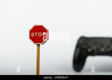 Un gros plan d'un panneau d'arrêt de jouet en bois se trouve dans la mise au point nette, avec un contrôleur de jeu vidéo légèrement flou en arrière-plan sur une surface blanche Banque D'Images