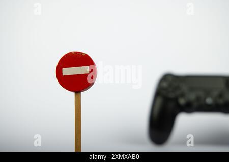 Un jouet en bois « No Entry » signe est bien en évidence avec une manette de jeu floue en arrière-plan, placé sur un fond blanc propre, accentué Banque D'Images