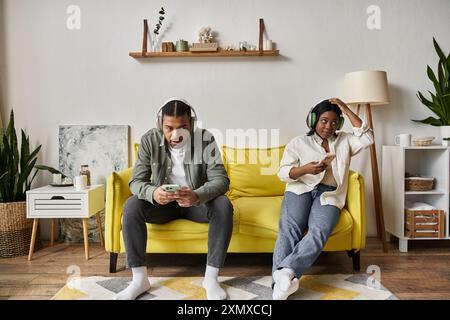 Un couple afro-américain aimant passe du temps ensemble sur un canapé jaune dans leur maison. Banque D'Images