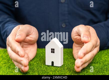 L'homme protège la maison avec ses mains. Protéger la propriété contre les menaces et les dangers. Assurance immobilière, protection juridique des droits de propriété. Banque D'Images