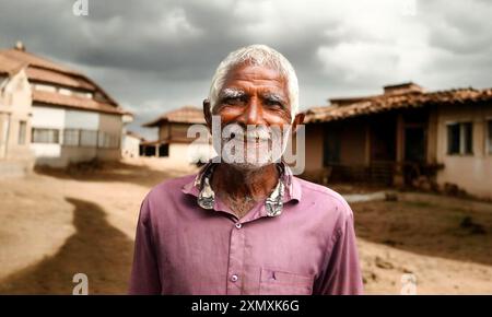 Portrait d'un vieux villageois indien souriant et regardant la caméra derrière le quartier des bidonvilles. Banque D'Images