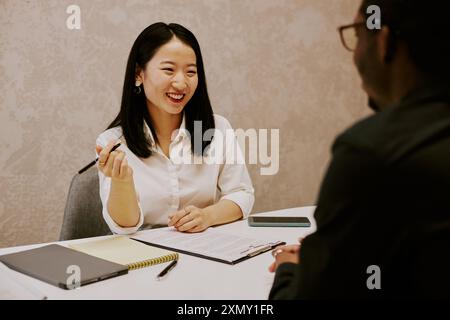 Sympathique jeune responsable des ressources humaines asiatique souriant lors d'un entretien avec un candidat noir méconnaissable, au-dessus de l'épaule Banque D'Images