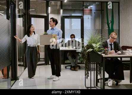 Grand plan d'un jeune responsable des ressources humaines asiatique sympathique faisant une démonstration de bureau à un nouvel employé, espace de copie Banque D'Images
