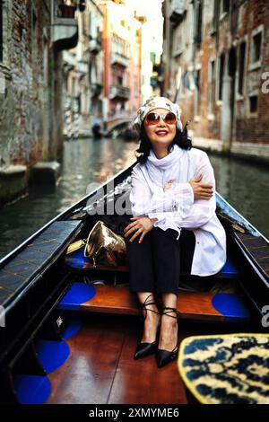 Une femme heureuse profitant d'une balade en gondole entre de vieux bâtiments pittoresques sur un canal vénitien, à Venise, en Italie Banque D'Images