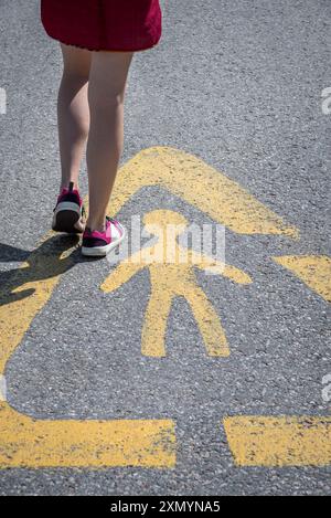 Fille marchant à travers le signe de la rue attention enfants sur Asphalt Road. Attention aux enfants ! Banque D'Images