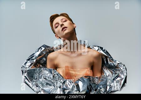 Une femme drapée dans du papier d'argent, un témoignage de la mode durable. Banque D'Images