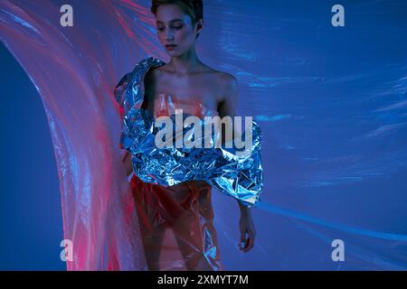 Une femme portant un vêtement de mode durable argenté pose devant un fond bleu et rose. Banque D'Images