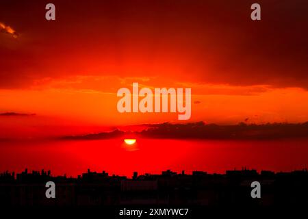 Ciel nuageux au-dessus des toits de la ville. Le soleil couchant peint le ciel d'un rouge profond Banque D'Images