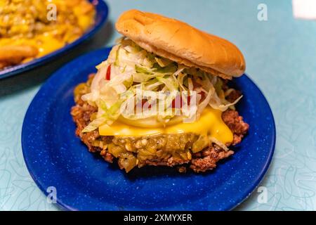 Vue rapprochée du hamburger avec fromage, laitue et tomate sur plaque bleue dans le dîner local. Banque D'Images