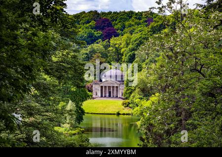 Le temple du Panthéon vu à travers une brèche dans la forêt de l'autre côté du lac à Stourhead Gardens, Wiltshire, Angleterre, Royaume-Uni Banque D'Images