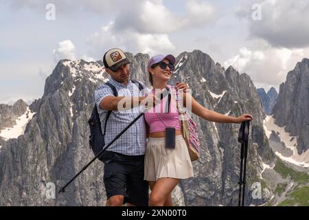 Un jeune couple, un homme et une femme debout sur fond de montagnes enneigées. L'homme montre la direction où aller. Ils sont souriants et apprécient. Banque D'Images