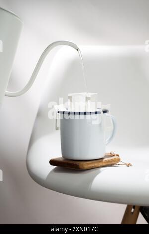 Cette photographie illustre le processus d'égouttement de l'eau chaude à travers un sac de café pré-fait dans une tasse en céramique blanche avec des bords bleu foncé, placé Banque D'Images