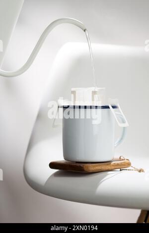 Cette photographie illustre le processus d'égouttement de l'eau chaude à travers un sac de café pré-fait dans une tasse en céramique blanche avec des bords bleu foncé, placé Banque D'Images