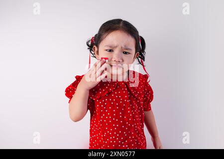 Une jeune fille asiatique en bas âge exprime un esprit pour le jour de l'indépendance indonésienne, portant une chemise rouge, debout sur un fond blanc Banque D'Images