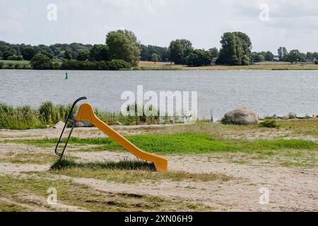 Arnis, Allemagne. 24 juillet 2024. Un toboggan se dresse sur les rives du Schlei, inondé lors de la grave onde de tempête de la mer Baltique à l'automne 2023. La digue à Arnis a été percée sur une longueur de 60 mètres. Tout le long de la côte, des digues et des installations portuaires ont été endommagées ou détruites, et des maisons, des campings et des hôtels ont été dévastés. Le gouvernement de l'État a estimé les dégâts à environ 200 millions d'euros. Crédit : Frank Molter/dpa/Alamy Live News Banque D'Images