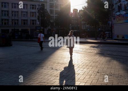 Une femme est contre-éclairée par le soleil levant lors de sa promenade matinale pour travailler dans les rues tranquilles d'Amsterdam, aux pays-Bas. Banque D'Images