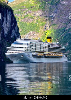 Geiranger fjord Norvège 10 juillet 2024, Un superbe bateau de croisière navigue dans les eaux calmes des fjords norvégiens, entouré de falaises imposantes et d'une végétation vibrante à l'aube. Banque D'Images