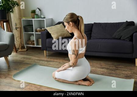 Une jeune femme en vêtements d'activité pratique le yoga sur un tapis dans un appartement moderne. Banque D'Images