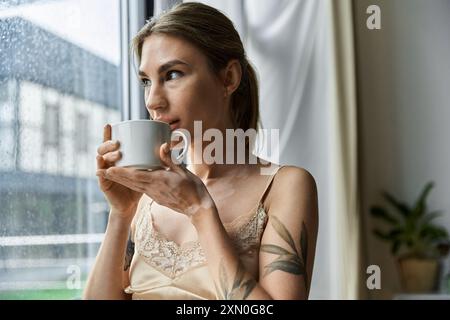 Une jeune femme atteinte de vitiligo sirote du café tout en regardant par la fenêtre un jour de pluie. Banque D'Images