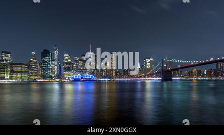 Vue sur le pont de Brooklyn et les gratte-ciel de Manhattan pendant l'heure bleue avec des reflets lumineux dans l'East River. Banque D'Images