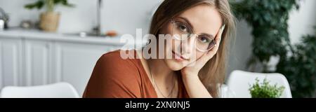 Une femme avec des lunettes et un doux sourire est assise dans une pièce ensoleillée. Banque D'Images