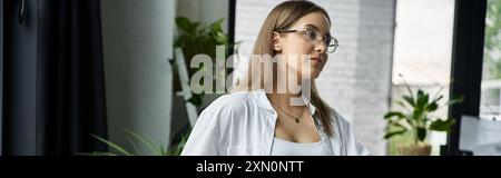 Une femme aux longs cheveux bruns et aux lunettes, portant une chemise blanche, regarde par une fenêtre. Banque D'Images