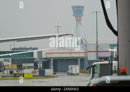 Aéroport d'Heathrow par une journée brumeuse de mai. Ailes d'avion et véhicules de support. La tour de contrôle au loin. Banque D'Images