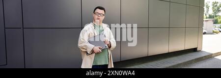 Un jeune homme atteint du syndrome de Down se tient dehors, tenant un ordinateur portable. Banque D'Images