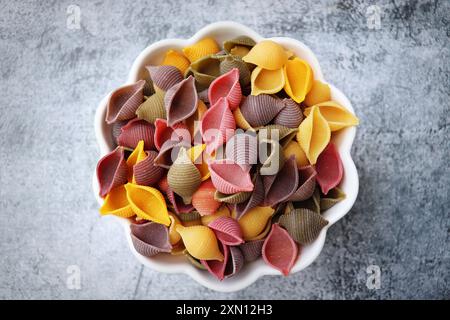 Fond de pâtes coloré. Vue de dessus des coquilles de pâtes cinq couleurs sur fond de pierre blanche. Pâtes au curcuma, aux épinards, à la betterave et à la carotte noire. Banque D'Images