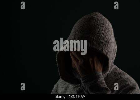 Gros plan portrait d'un homme mystérieux portant des lunettes de soleil et un sweat-shirt à capuche couvrant la tête avec les mains sur le visage. Isolé sur fond sombre. Banque D'Images