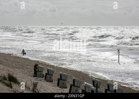 Strandkörbe und Spaziergänger am Strand von Westerland, Sylt DEU, Deutschland, Sylt, Westerland : Das Bild zeigt einen weiten Strandabschnitt in Westerland auf Sylt. IM Vordergrund sind mehrere Strandkörbe zu sehen, und eine person geht entlang des Strandes. Die Nordsee ist rau mit hohen Wellen und der Himmel ist bedeckt. Westerland Sylt Schleswig Holstein Deutschland *** chaises de plage et marcheurs sur la plage de Westerland, Sylt DEU, Allemagne, Sylt, Westerland L'image montre une large étendue de plage à Westerland sur Sylt au premier plan sont plusieurs chaises de plage, et une personne se promène le long Banque D'Images