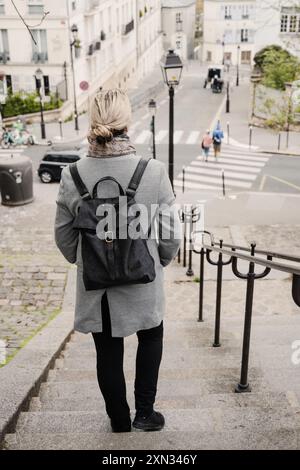 Une femme descend un escalier dans une rue calme de Paris, capturée par derrière. Paris, France Banque D'Images