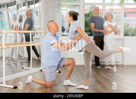Femme âgée souriante portant des vêtements de sport dansant en couple et la formation ballet arabesque pose avec partenaire pendant le cours de groupe au salon de danse Banque D'Images