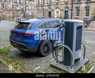 Edimbourg, Écosse, 07.17.2024 : voiture électrique Blue Mercedes rechargeant ses batteries sur un point de recharge dans une rue pavée d'Edimbourg Banque D'Images