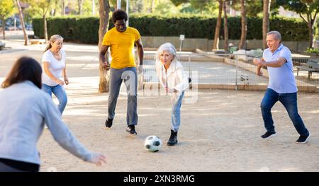 Joyeux amis multinationaux jouant au football sur un terrain de jeu sablonneux lors d'une chaude soirée de printemps Banque D'Images