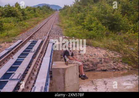 Un adolescent de race mixte, un touriste domestique, est assis sur un pont pour le train de bambou pendant COVID - 19. Province de Battambang, Cambodge. © Kraig Lieb Banque D'Images