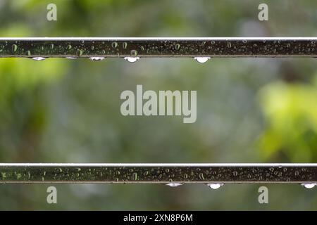 Gouttes de pluie sur le tuyau en acier dans le balcon. Gouttelettes d'eau de pluie sur le tuyau en acier dans les jours de pluie avec fond de nature vert flou et lumière bokeh. Banque D'Images