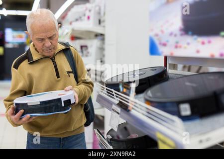 Senor homme retraité achetant aspirateur robotique dans la salle d'exposition de stor d'appareil électrique Banque D'Images