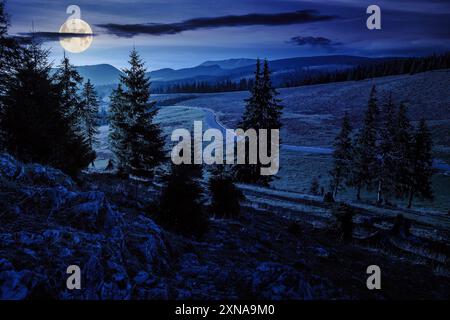 paysage de montagne d'automne la nuit. la route asphaltée serpente à travers les montagnes et passe le pré près de la forêt de conifères à feuilles persistantes. magnifique campagne Banque D'Images