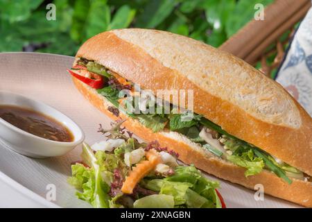 Une baguette fraîchement cuite remplie d'ingrédients salés, accompagnée d'une salade d'accompagnement et d'un petit bol de sauce trempette Banque D'Images